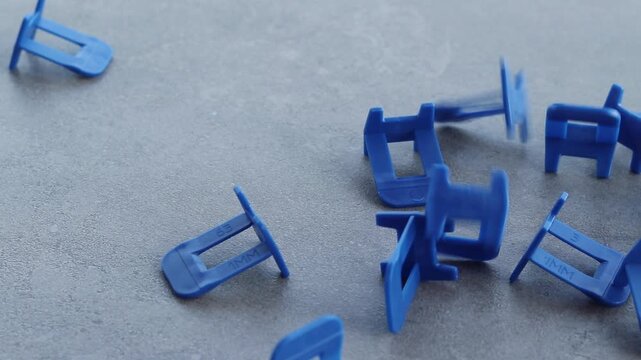 Blue plastic clamps for tile leveling system, close-up. Professional consumables for laying ceramic and porcelain tiles. A large number of blue plastic clamps fall on a gray surface. Repair