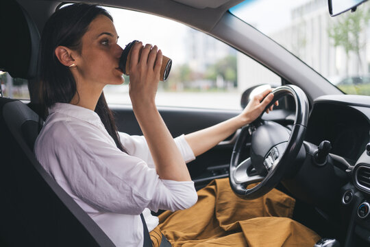 Woman drinking coffee while driving a car on daily commute