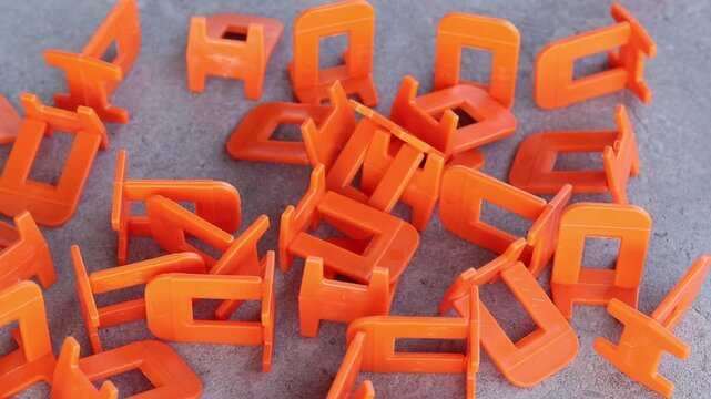 Orange plastic clamps for tile leveling system, close-up. Professional consumables for laying ceramic and porcelain tiles. A large number of orange plastic clamps fall on a gray surface. Repair