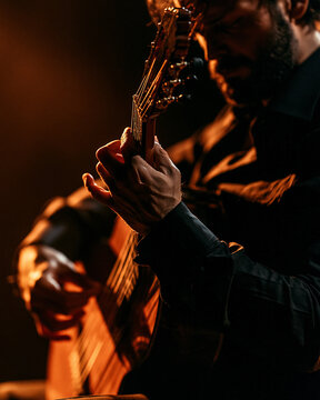 Male guitarist playing acoustic guitar in a live concert close-up with pensive expression and stage light silhouette