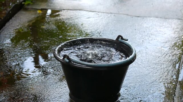 Heavy precipitation drops fall into a dark container, demonstrating meteorological rainwater harvesting methods, domestic hydrology conservation, and natural liquid resource sustainability