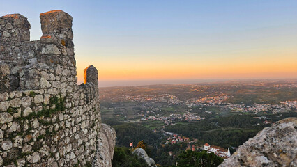 Ancient Moorish castle wall foregrounding a vast panoramic view of Sintra city and the distant ocean horizon illuminated by golden hour light © Dark Artistic