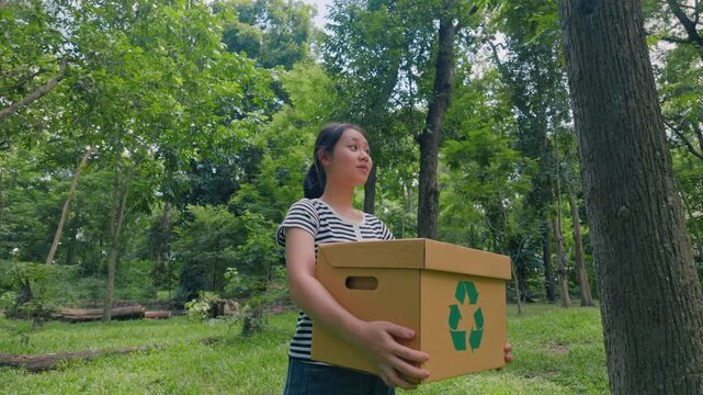 Asian woman holding recycling box on green nature forest background. Sustainable environment concept. Recycle plastic free of zero waste, from waste to environment. 