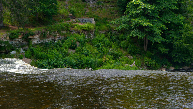 Keila Joa waterfall water flowing over a limestone edge with lush green vegetation and trees on the steep riverbank under natural daylight