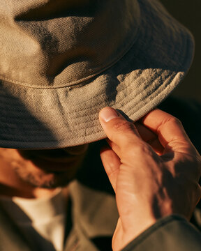Man touching bucket hat close-up in outdoor lifestyle photography with natural light and muted earth tone style