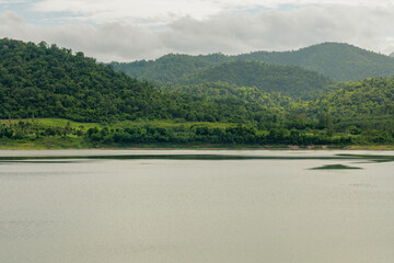 Fototapeta premium Scenic View of Huai Tha Khoei Reservoir Surrounded by Lush Green Mountains During the Rainy Season in Ban Kha District, Ratchaburi, Thailand
