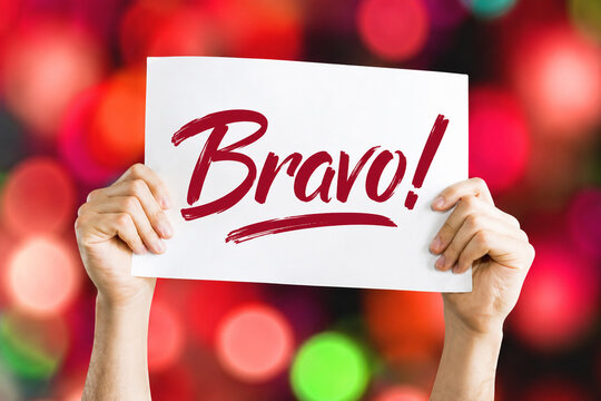 Hands holding sign with handwritten bravo text over blurred colorful bokeh lights background.
