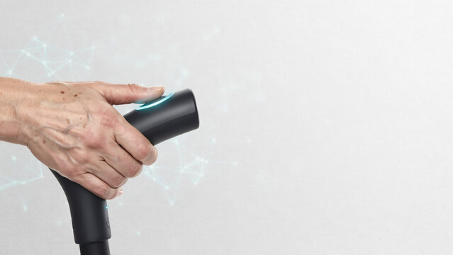 Senior hand holding smart walking cane with glowing blue button interface