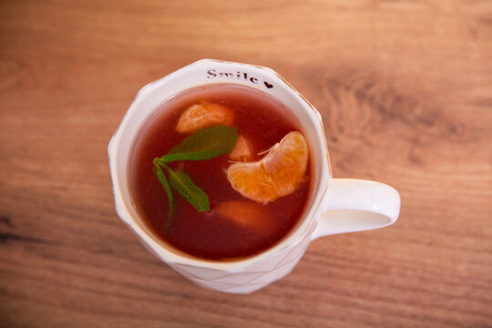 Cup of hot tea with fresh mint leaves and mandarin slices on a wooden table. Warm aromatic beverage with citrus fruit, viewed from above.