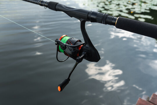Fishing rod and spinning reel closeup, angler tackle equipment, active sportfishing gear and line over lake water.