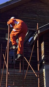 Construction worker descending metal scaffolding at residential building renovation site while wearing safety helmet