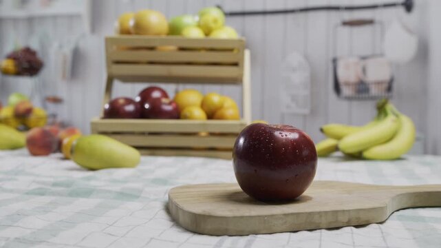 Tracking shot of wet red apple on counter with other fruit behind it