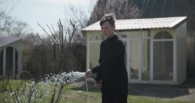 Kid Waters Plants in Garden Near House. Caucasian Boy Help Working Around Backyard. 4K 10-bit