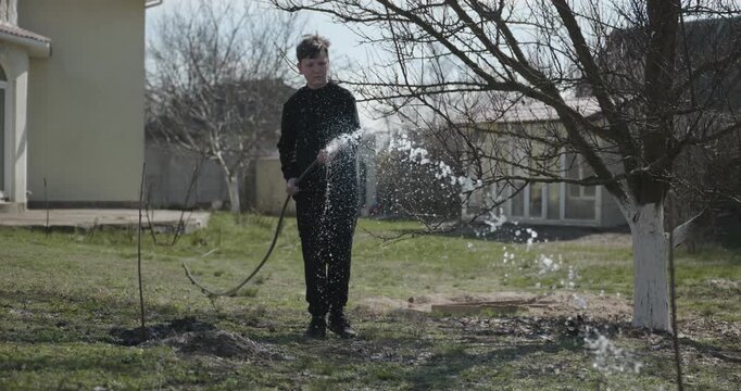 Kid Waters Plants in Garden Near House. Caucasian Boy Help Working Around Backyard. 4K 10-bit