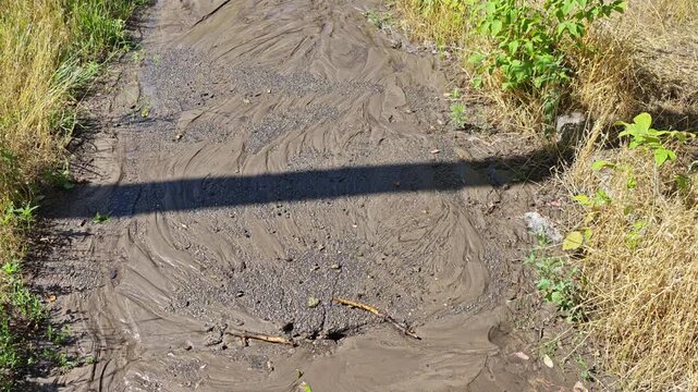 Wet mud and silt covering an asphalt pedestrian pathway with a straight shadow cast across the sludge.