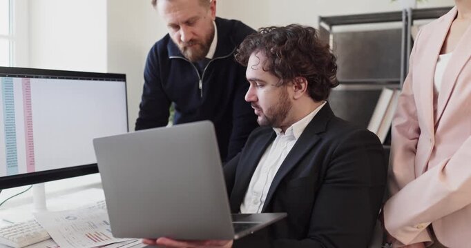 Managers and analysts in team meeting planning. Colleagues examine data on laptop and desktop, compare spreadsheets and discuss audit goals with clear strategy. Clear audit data for strategy.