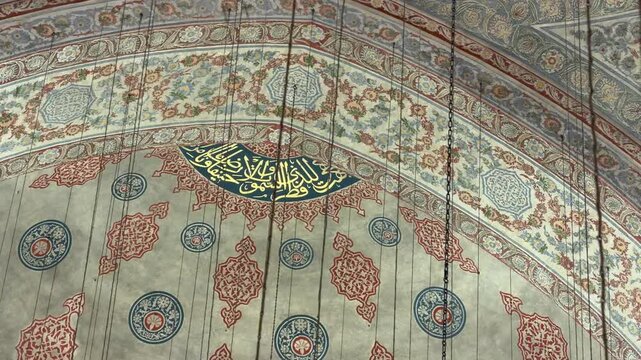 Slow tracking shot capturing the intricate hand-painted floral motifs and golden Arabic calligraphy on the vaulted ceiling of a historic mosque in Istanbul, Turkey.