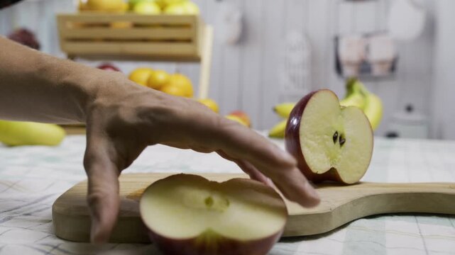 Woman's hand using knife to cut delicious apple into slices on cutting board in kitchen - closeup