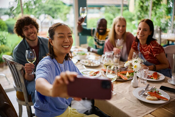 Obraz premium Happy friends having fun while gathering for lunch in restaurant and taking selfie.