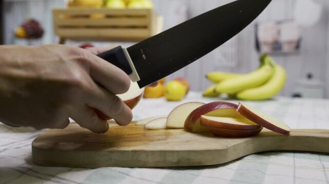 Tracking shot of person cutting apple into slices with sharp knife on cutting board - closeup