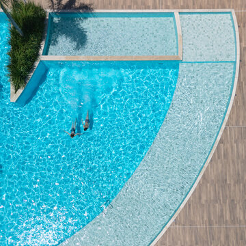 Two kids swimming in clear blue pool during sunny summer vacation. This aerial view captures family,  friends, fun, and recreation at resort, relaxation and joyful outdoor moments.