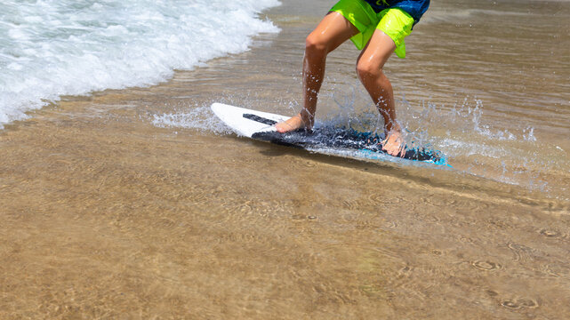 Young boy running, jumping on skimboard and sliding by shallow water on sunny sea beach. Skimboarding, childhood adventure, active lifestyle, watersports, summer vacation and fun outdoor activities.