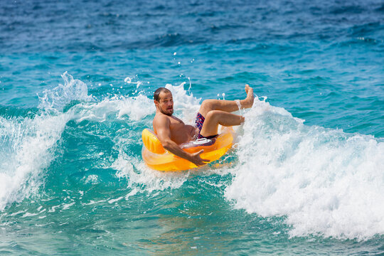 Man falling off inflatable ring while playing in ocean waves. Fun, energetic beach moment captured mid-splash. Ideal for summer vacation, tropical holiday, joy, active water recreation, sea adventure