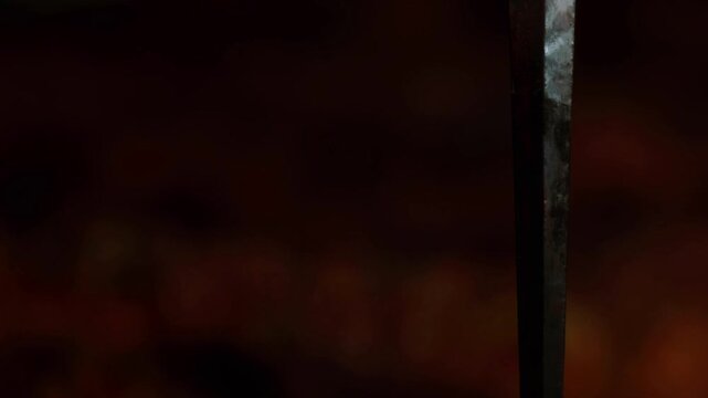 A dagger is stuck in the ground with a dark surface. The background shows blurred shapes and colors that suggest a nighttime setting. The scene has a mysterious atmosphere.