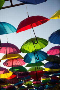 Colorful umbrellas hanging in rows above an outdoor walkway, vibrant decorative display, creative background, summer festival.