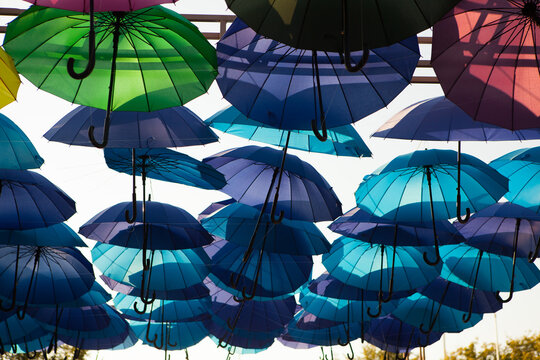 Blue and turquoise umbrellas form a layered canopy overhead, colorful outdoor decoration, creative festival background, summer travel theme.