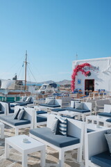 Fototapeta premium Stylish waterfront lounge in Naousa, Paros, Greece, overlooking the harbor with white Cycladic architecture, blooming bougainvillea, and a relaxed Mediterranean atmosphere.