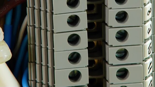 Close-up view of electrical wires expertly connected to grey terminal blocks and a shining brass busbar inside a detailed industrial control panel. The setup shows meticulous work.