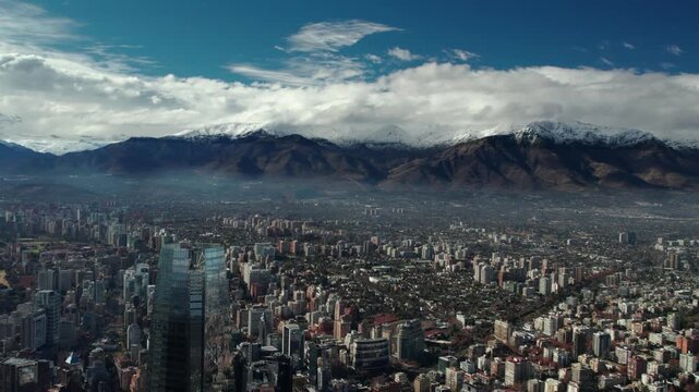 Santiago, Chile - July 18, 2026: Aerial drone view flying above the Costanera Center after rainfall, featuring a crystal-clear skyline, dramatic cloud formations and the snow-covered Andes Mountains s