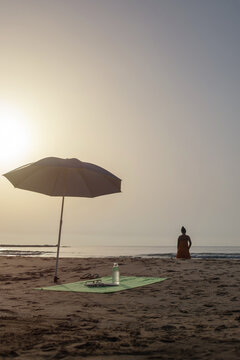 Vertical beach umbrella with book and woman looking at sea