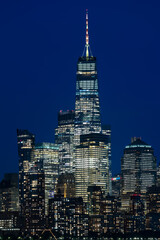 Obraz premium Vertical night view of downtown Manhattan featuring brightly lit high rise skyscrapers against a deep blue evening sky in New York.