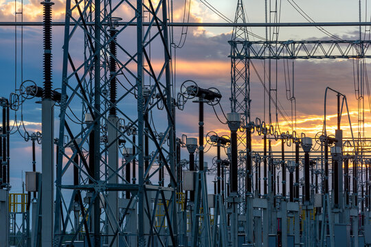 An electrical substation featuring steel towers, transformers, and power lines against a golden sunset sky in Villa Hayes, Paraguay.