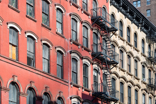 Facade of traditional red and beige brick apartment buildings with classic black fire escapes and arched windows in the historic Tribeca neighborhood of Manhattan, New York.