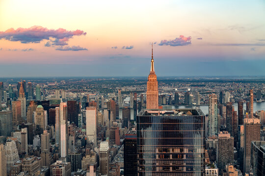 An impressive panoramic view of Manhattan at sunset looking East toward Queens, highlighting the glowing facade of skyscrapers in New York City.
