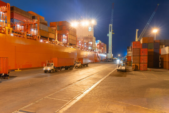 Loading and unloading of containers on a large cargo ship at a port terminal during night operations with bright illumination.