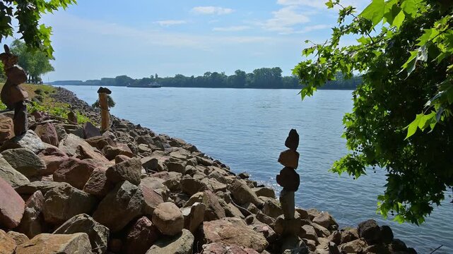 Steine auf einem Flussufer bei strahlendem Sonnenschein und ruhigem Wasser, umgeben von gr&uuml;nem Laub, Rhein, Eltville am Rhein, Rheingau, Hessen, Deutschland
Steine auf einem Flussufer bei strahlendem 