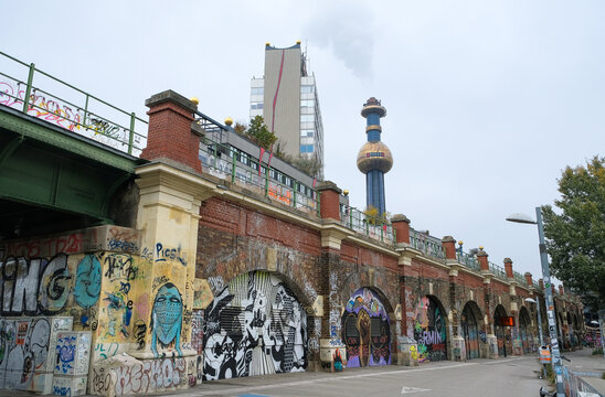 Vienna, Austria; October 30, 2022;  Urban Vienna scene with graffiti-covered brick viaduct and the iconic Hundertwasser Spittelau Waste Incineration Plant with colorful chimney.