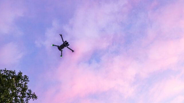 Modern drone flying high in the colorful twilight sky with soft clouds