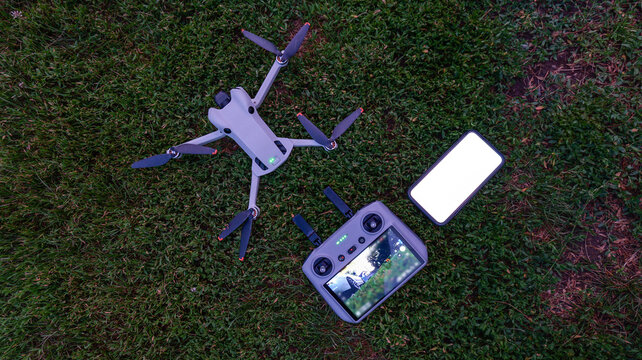 Modern drone and remote controller with smartphone laid out on green grass