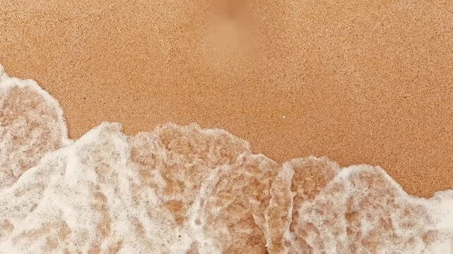 V&iacute;deo cenital art&iacute;stico de espuma marina avanzando sobre arena dorada con textura suave y minimalista.