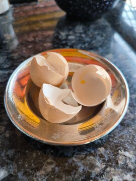 Broken brown eggshell halves on decorative metallic plate, reflective countertop highlighting everyday kitchen detail.