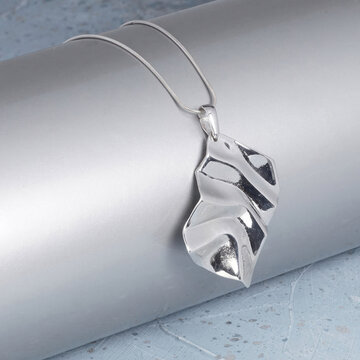 Close-up professional photo of an elegant silver pendant necklace adorned with shimmering clear crystals on a textured light surface. Ideal for jewelry retail and fashion marketing.