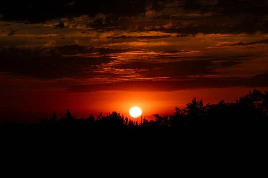 Fiery sunset above silhouetted forest beneath dramatic storm clouds