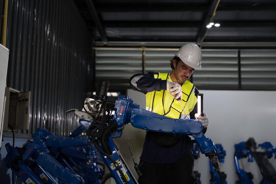Male engineer wearing uniform, white hard hat and gloves repair automatic robotic arm for welding. Male technician inspecting quality automatic welding robot arm machine with hand tools