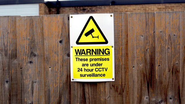 CCTV surveillance warning sign, security camera notice on wooden fence, 24 hour protection concept
