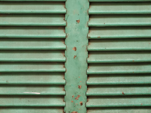 Close-up of weathered teal green window shutters with peeling paint and horizontal slats